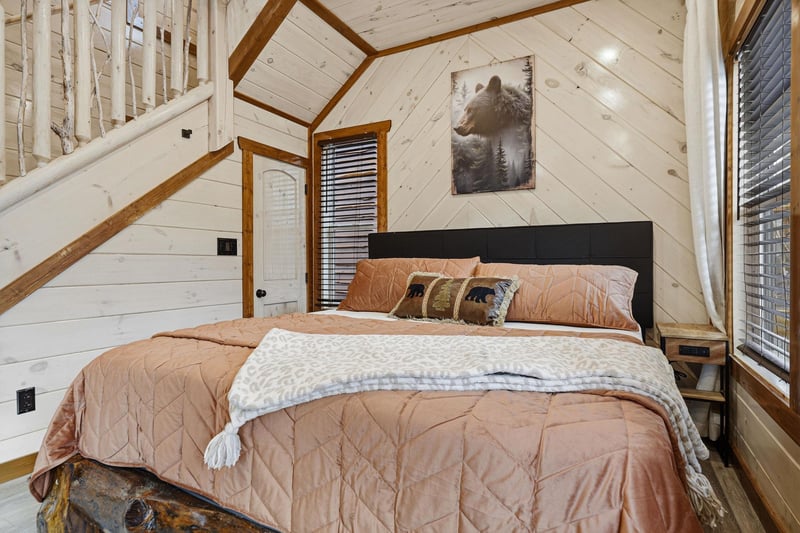 Drift off to sleep surrounded by rustic charm, where soft bedding meets woodland elegance beneath soaring timber ceilings in your cozy retreat.