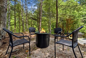 A tranquil forest setting surrounds this outdoor seating area with a cozy fire pit, perfect for peaceful evenings under the trees.