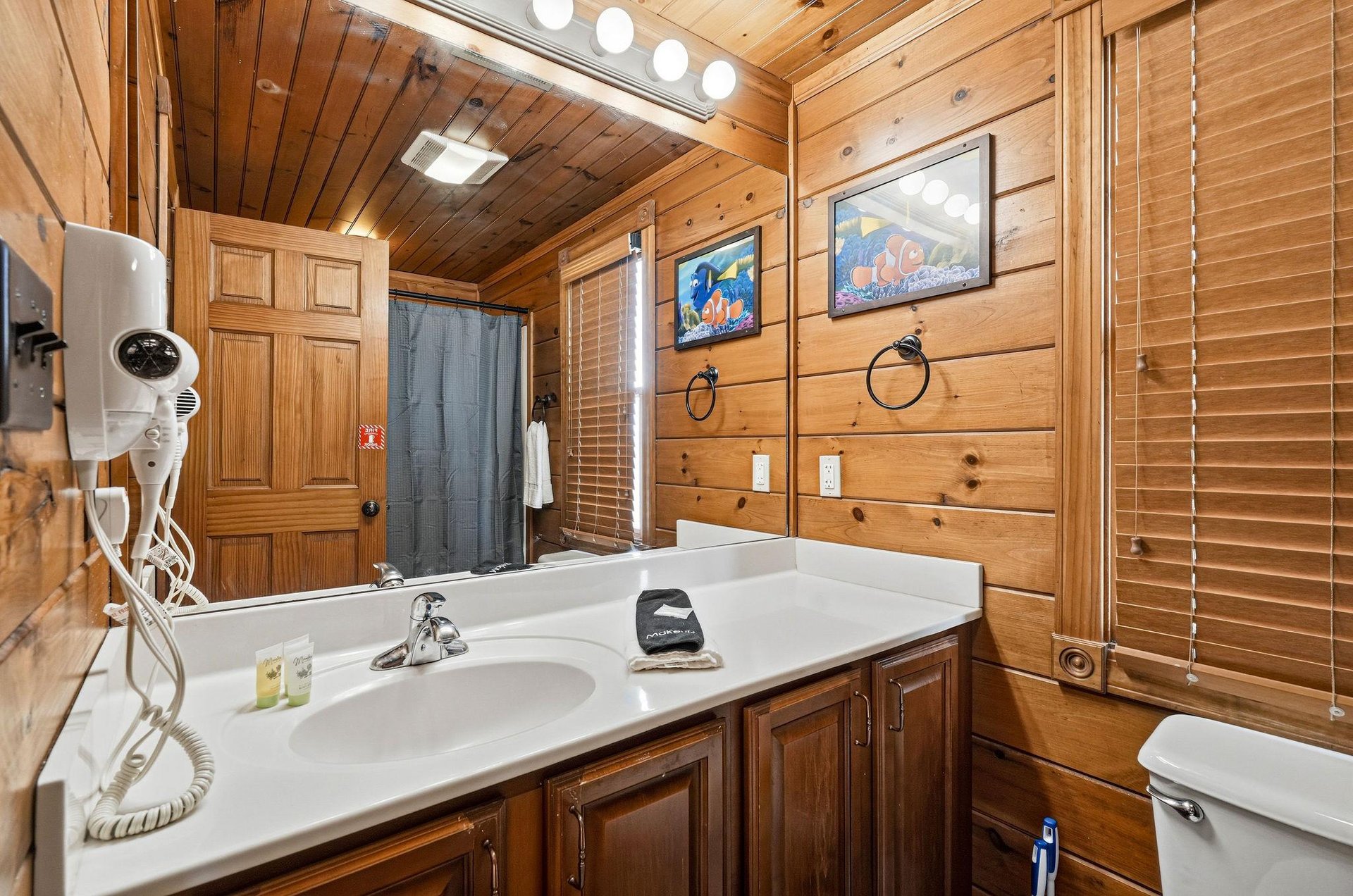 Step into your cozy cabin bathroom with warm wood walls, plenty of counter space, a skylight brightening your mornings, and cheerful oceanthemed art that adds a splash of character.