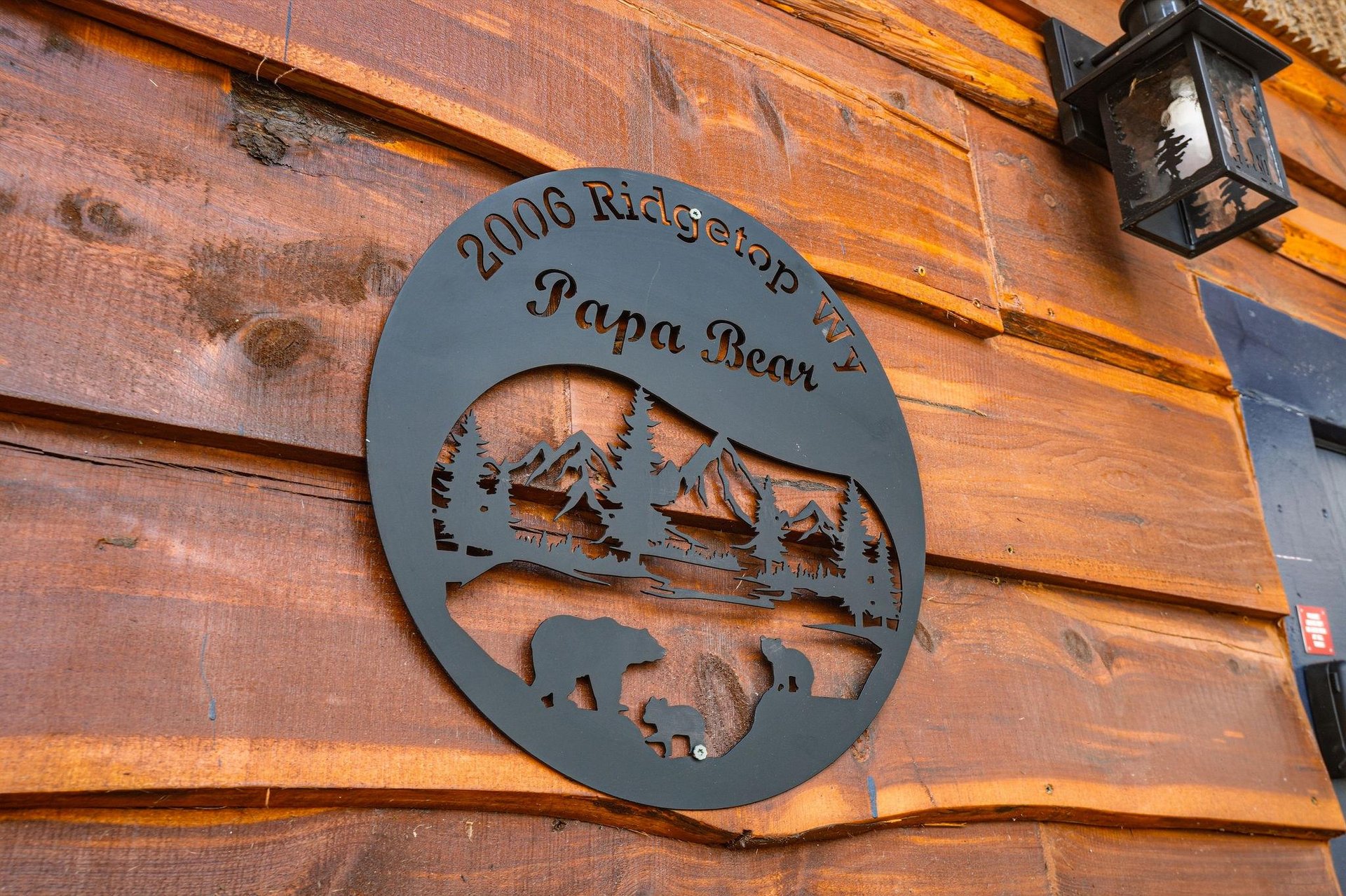 Charming mountain cabin entrance features custom metal signage with wilderness silhouettes against warm wood siding.