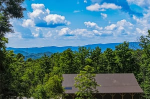 Property set among rolling blue mountains and lush forest, with dramatic cloud formations overhead creating a scenic natural backdrop.