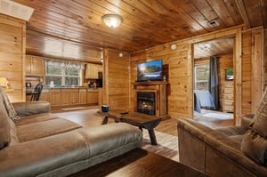 Relax in this cozy log cabin living room with crackling fireplace, plush leather seating, and warm wood throughout your mountain getaway.