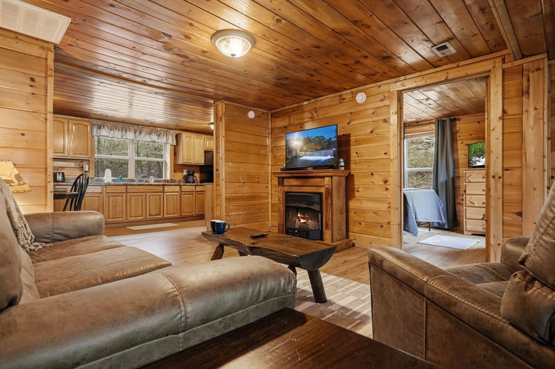 Relax in this cozy log cabin living room with crackling fireplace, plush leather seating, and warm wood throughout your mountain getaway.