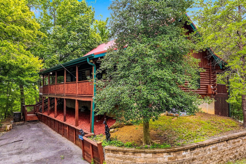 A charming log cabin retreat nestled among vibrant spring foliage, offering a peaceful wooded escape with spacious decks and natural beauty all around.