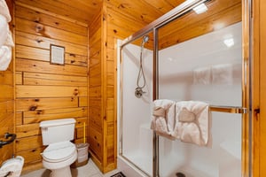 Cozy cabinstyle bathroom with warm pine walls, a gleaming shower, and fresh towels waiting for you.