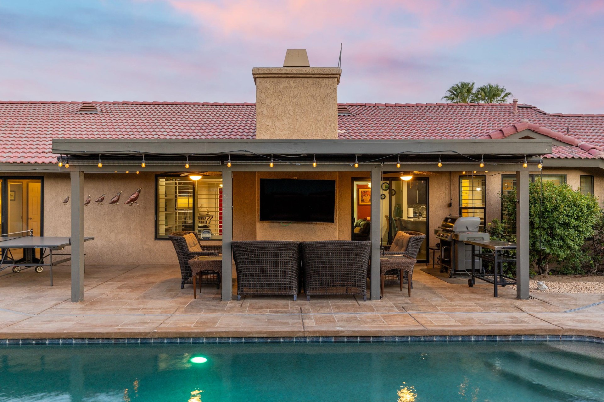 Covered patio with ample outdoor seating, BBQ grill, and flatscreen TV.
