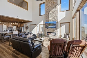 Unwind in your spacious living area featuring leather seating, a stunning stone fireplace, and floortoceiling windows that flood the space with natural light.