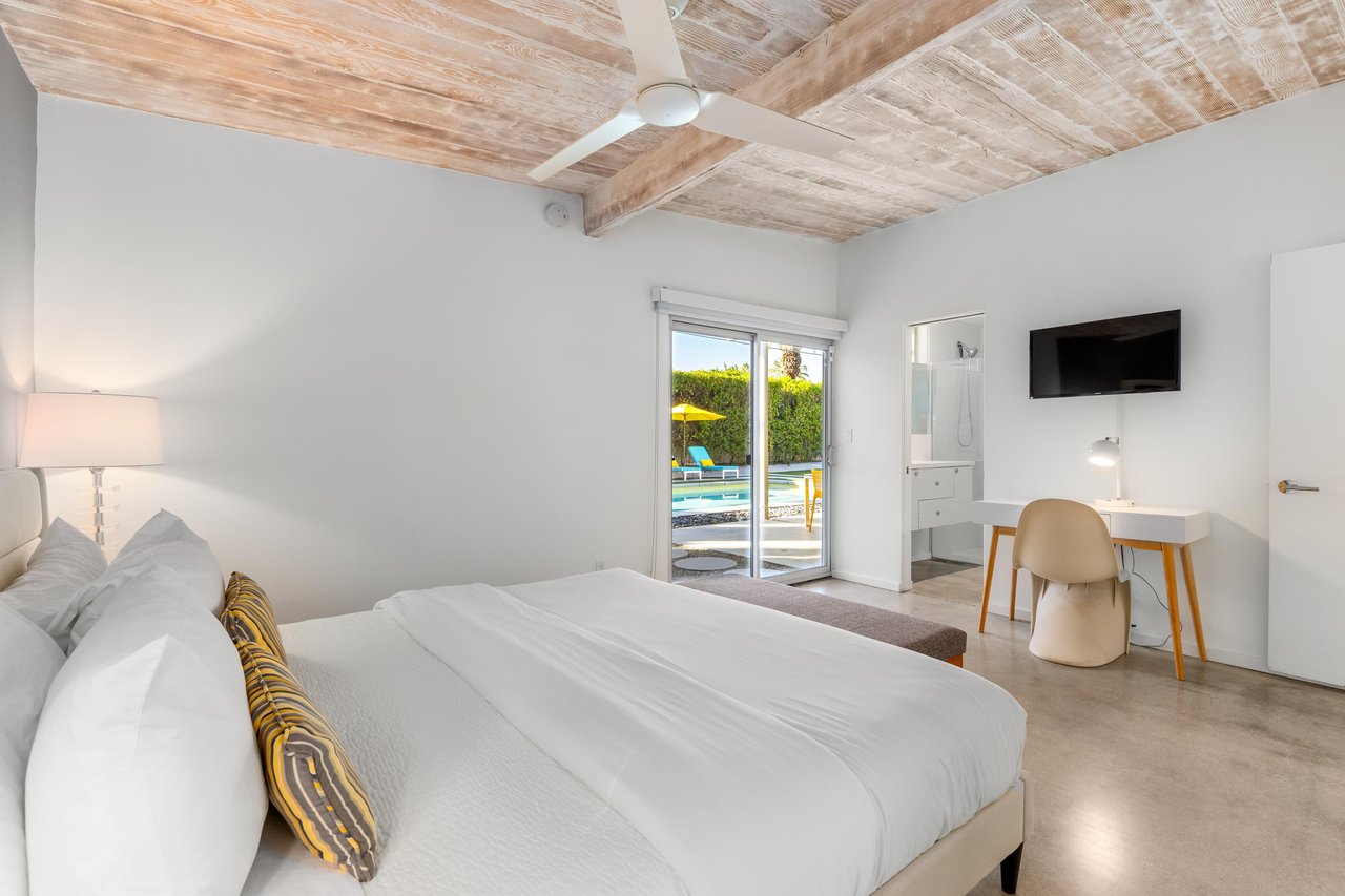 Relax in your serene bedroom with exposed wooden beams, modern amenities, and sliding doors opening to pool views.
