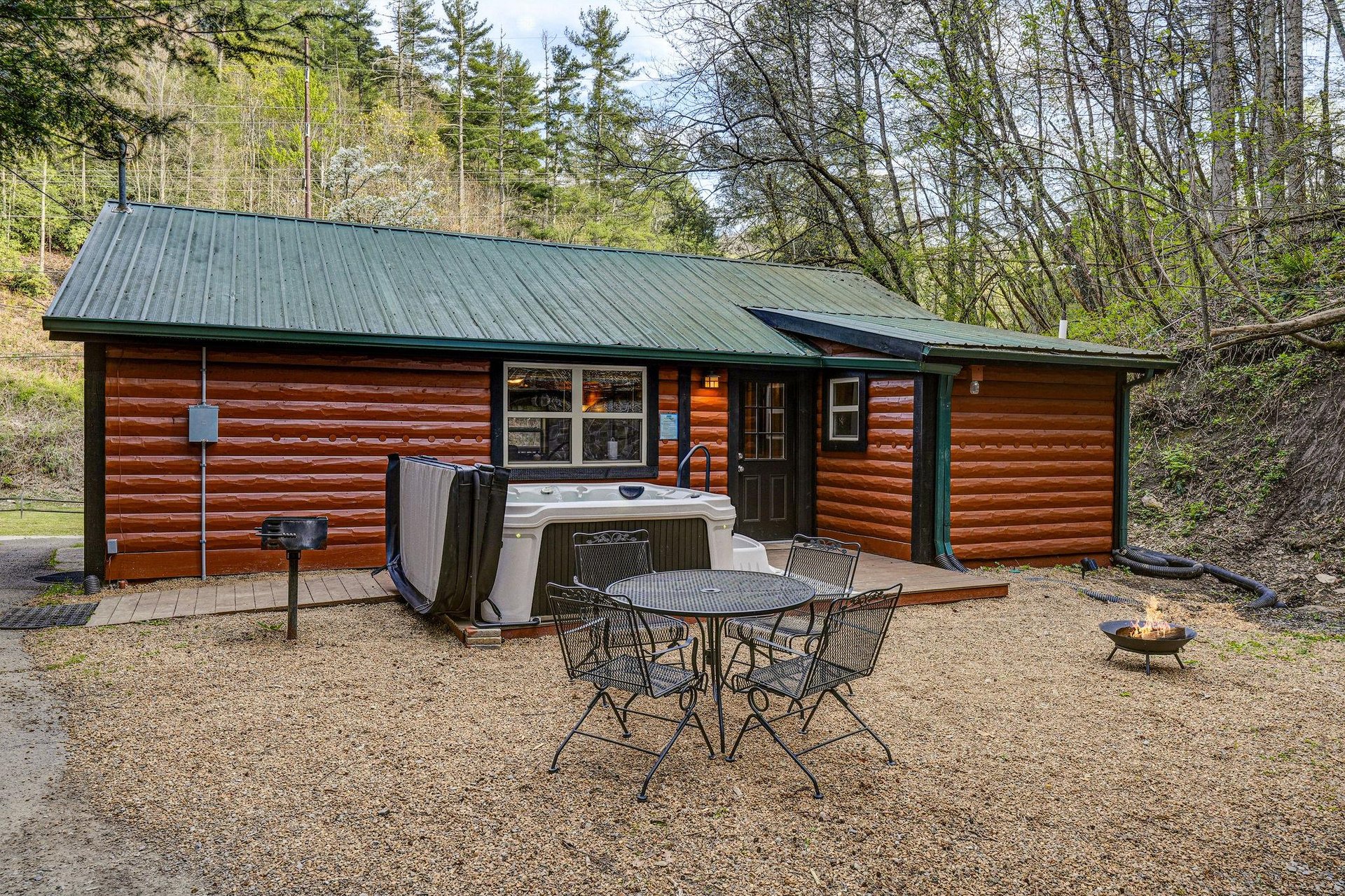 Rustic log cabin retreat surrounded by spring forest, featuring hot tub, outdoor dining, and fire pit for perfect mountain getaway relaxation.
