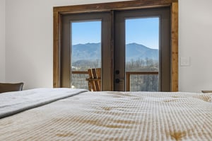 Wake up to breathtaking mountain views from your cozy bed, where rustic wood frames stunning vistas through French doors leading to your private balcony.