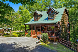 This charming log cabin is nestled in lush greenery, offering a peaceful mountain retreat with convenient parking and a welcoming front porch perfect for unwinding.