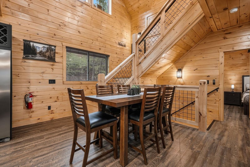 Gather around this rustic dining table where warm wood surrounds you and natural light flows through large windows, creating the perfect spot for memorable meals.