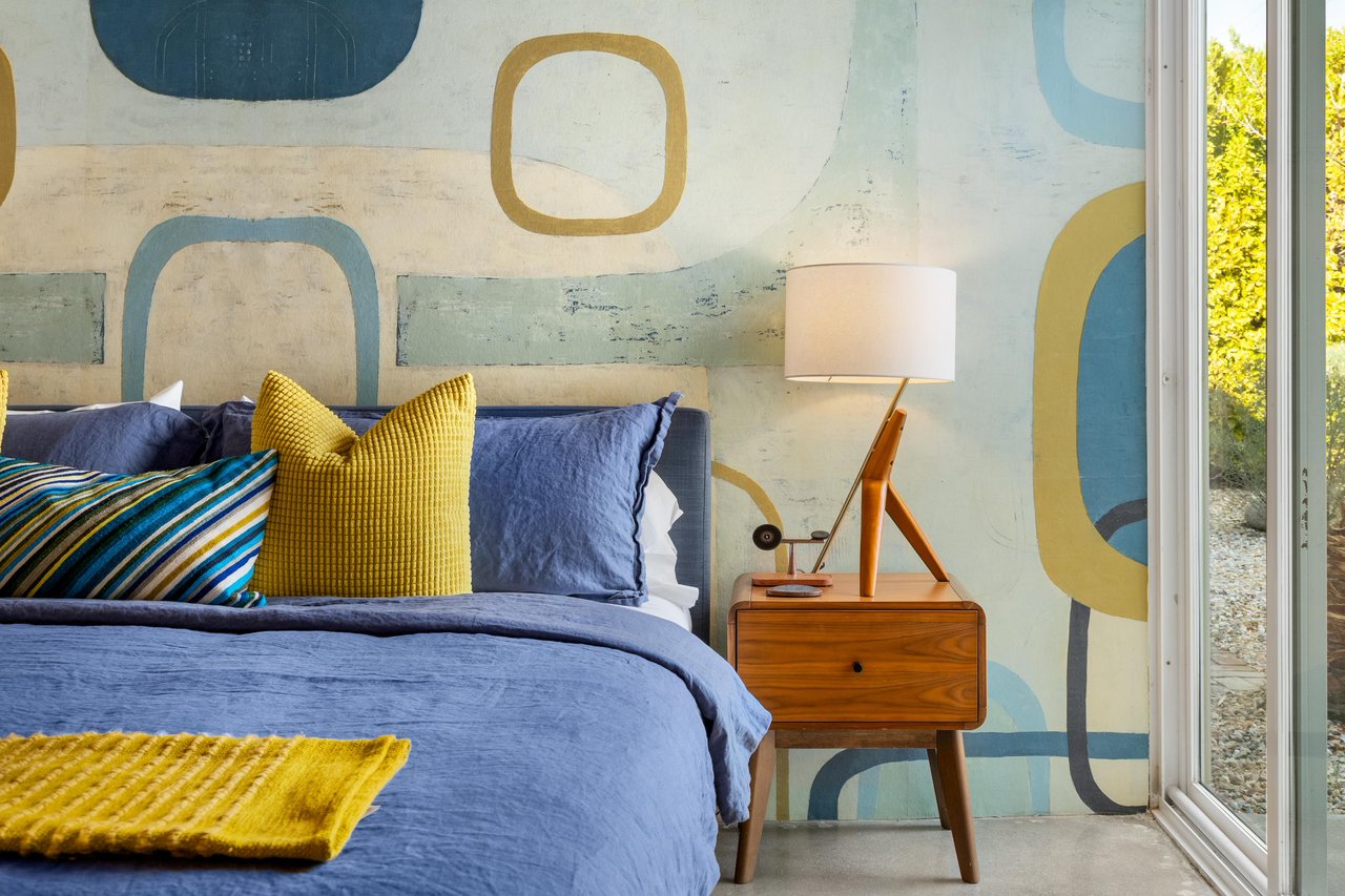 Wake up in style with vibrant blue linens and midcentury furnishings against playful geometric wallpaper.