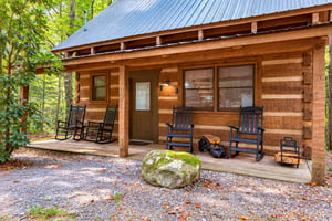 A welcoming log cabin nestled among tall trees offers a cozy front porch with rocking chairs, perfect for sipping morning coffee or unwinding after a day of exploring the forested surroundings.
