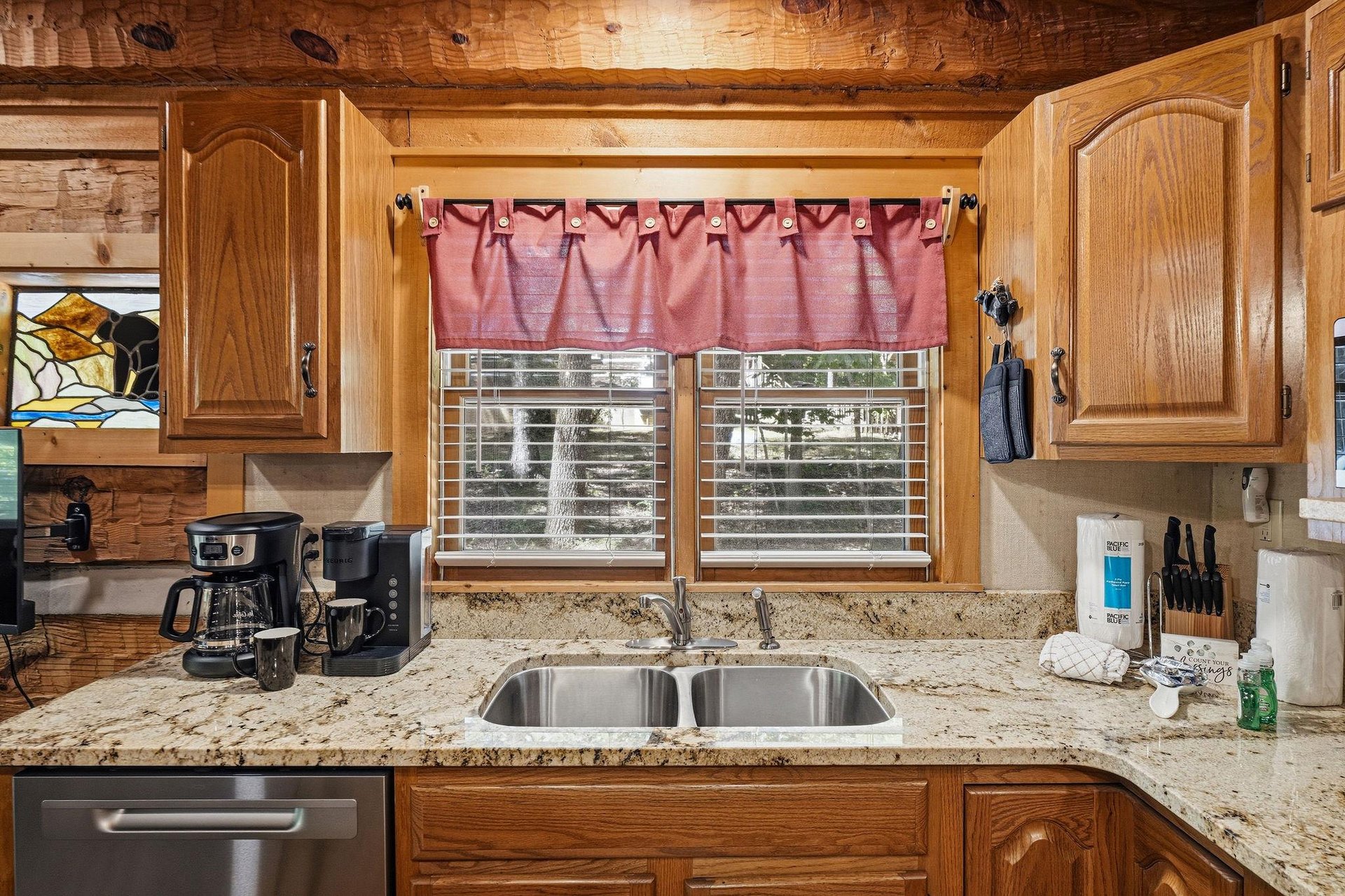 Your fully equipped kitchen features granite countertops, warm wood cabinets, and modern appliances—ready for preparing meals or brewing morning coffee with natural light streaming through the window.