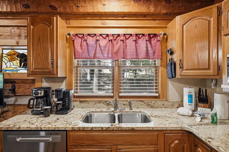 Your fully equipped kitchen features granite countertops, warm wood cabinets, and modern appliances—ready for preparing meals or brewing morning coffee with natural light streaming through the window.
