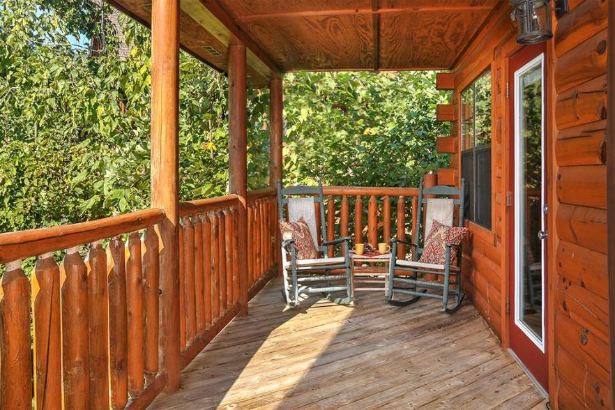 Covered deck with rocking chairs and wooded surround at Kick Back  Relax A 4 bedroom cabin rental located in Pigeon Forge