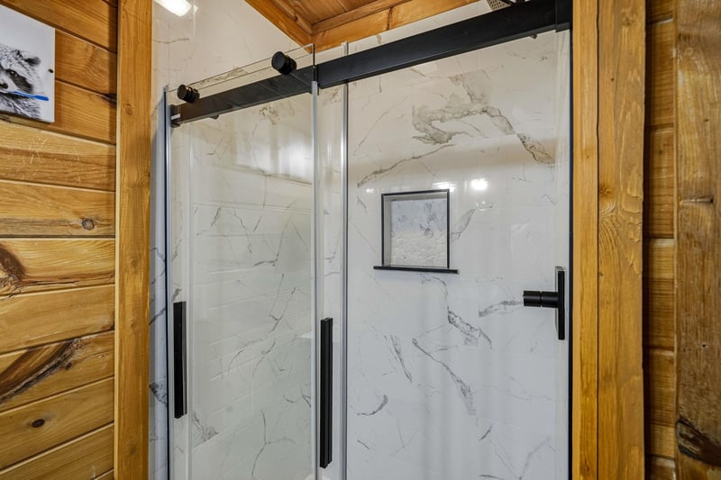 Your private shower awaits with elegant marblelook walls and sleek sliding doors in this warm woodpaneled retreat.