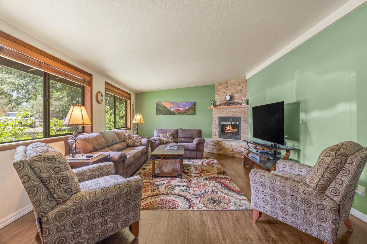 Spacious living room with a fireplace, flatscreen TV. and large windows with plenty of natural lighting.