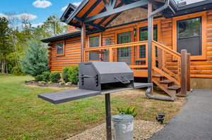 Charcoal grill ready for your outdoor cookout, just steps from the cabins inviting covered porch and surrounded by peaceful wooded scenery.