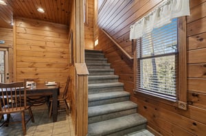 Step into this inviting cabin where warm wood surrounds you and natural light spills through the windows, highlighting cozy dining and upperlevel spaces perfect for your mountain retreat.