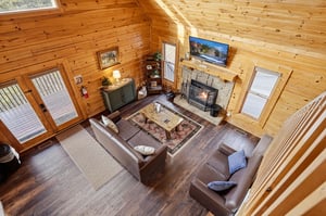 Relax in your cozy log cabin living room with warm wood walls, leather seating, and crackling stone fireplace creating the perfect mountain retreat atmosphere.