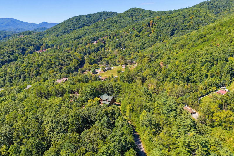 An aerial view showcasing the property nestled among lush, rolling mountains and dense forest. The stunning natural landscape and tranquil surroundings define this scenic retreat.