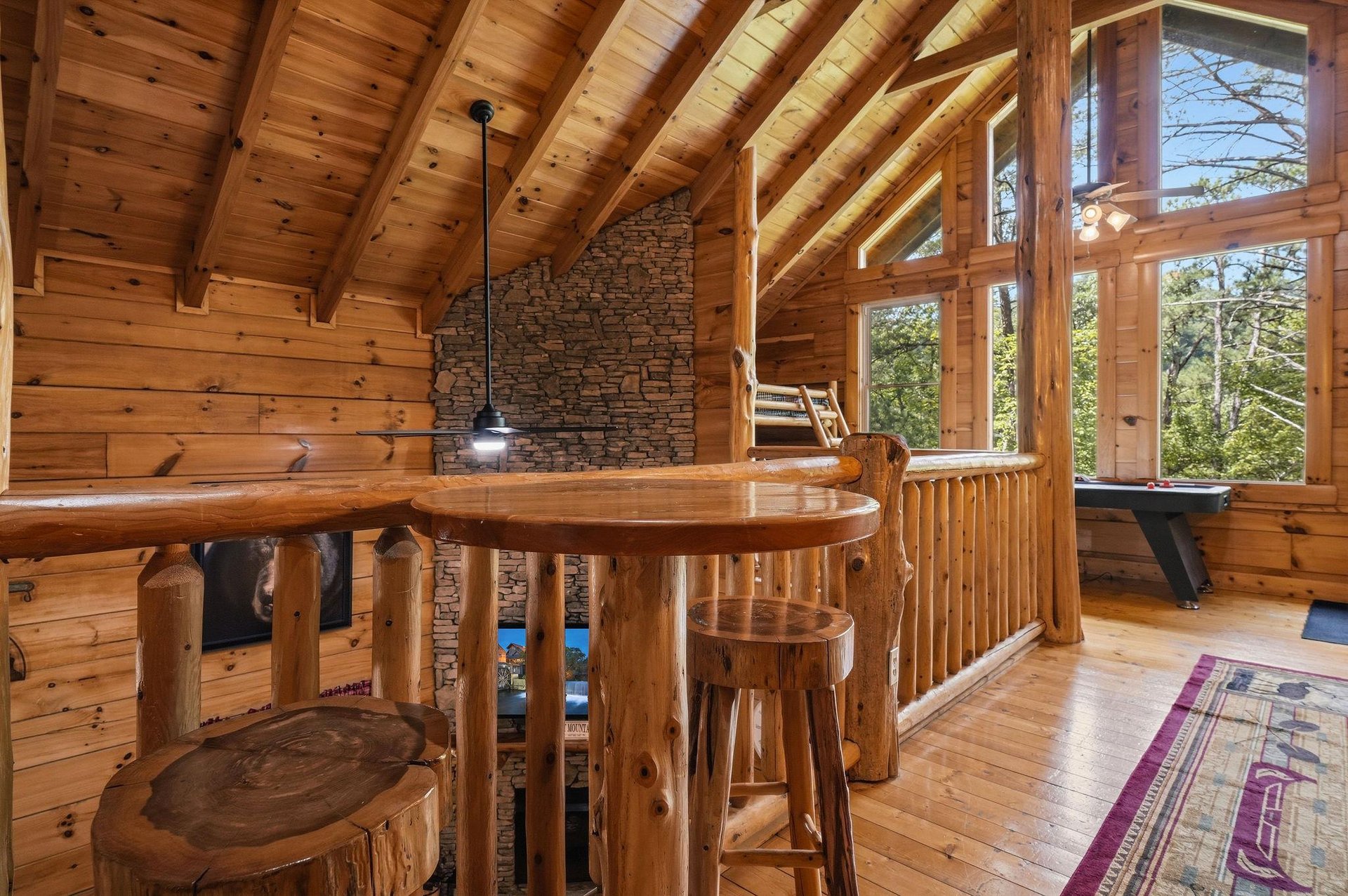 Gather around the rustic log bar in this soaring loft space, where warm wood tones and vaulted ceilings create the perfect retreat. Natural light pours in through towering windows framing forest views