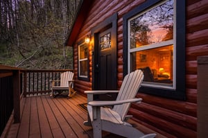 Cozy log cabin deck with Adirondack chairs where you can unwind while watching the sunset paint the sky in warm hues.