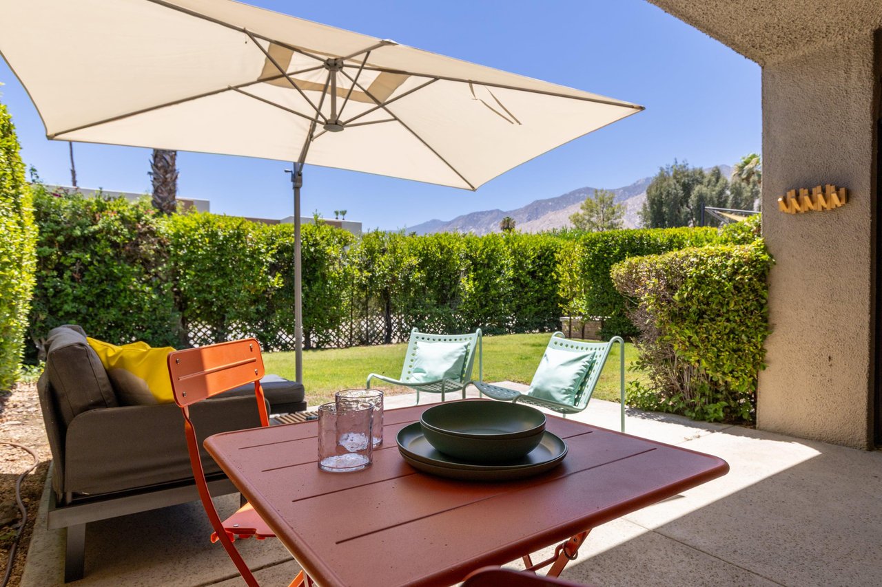 Back patio located off of the living room and primary bedroom featuring a table and chairs for morning coffee, umbrella, and ample outdoor seating.