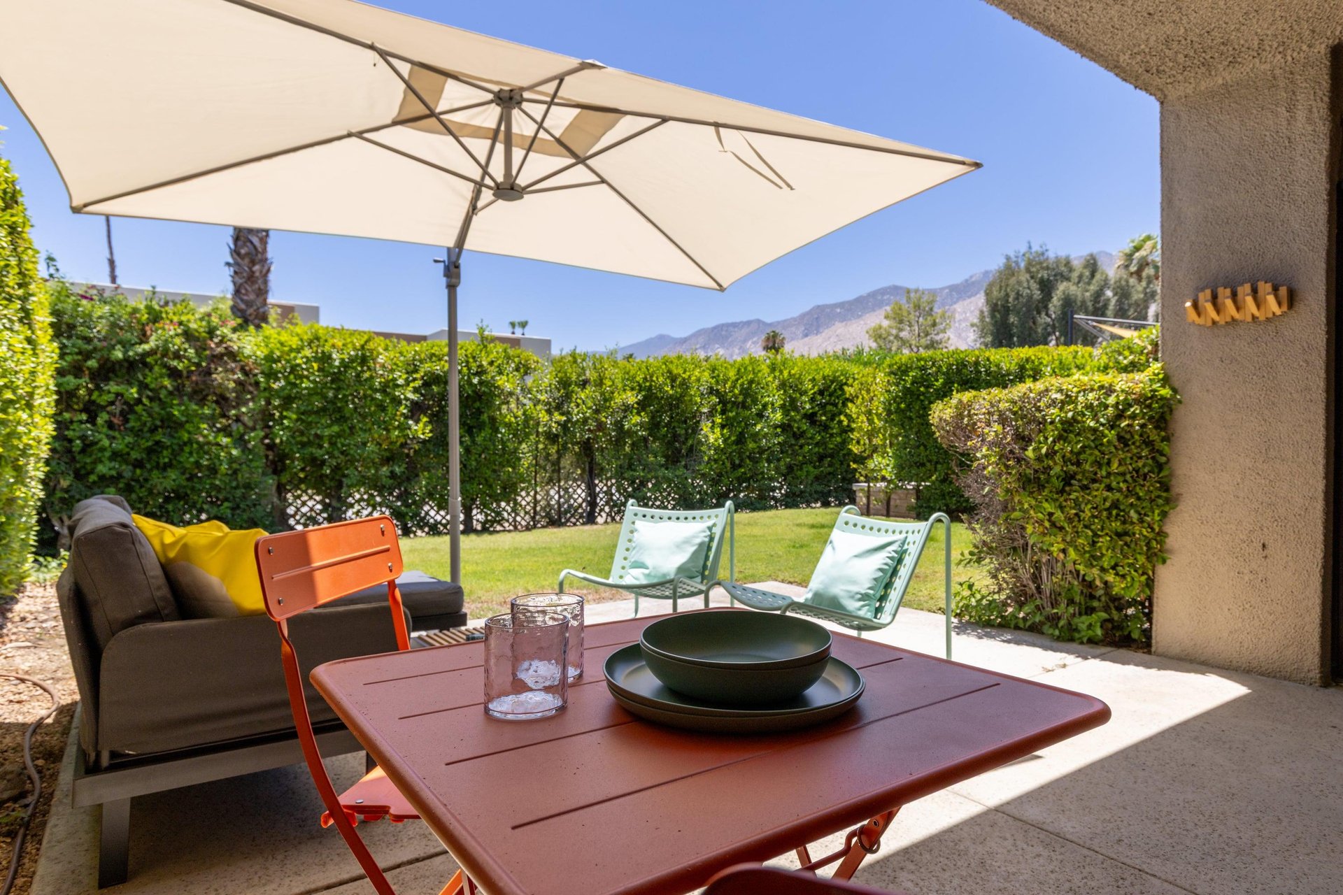 Back patio located off of the living room and primary bedroom featuring a table and chairs for morning coffee, umbrella, and ample outdoor seating.