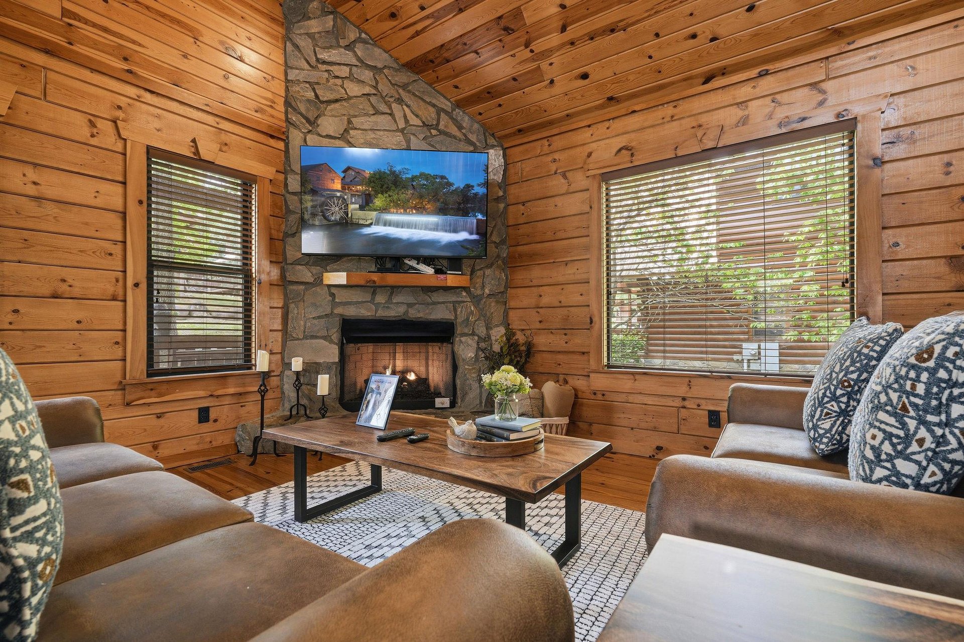 Cozy up in your rustic living room with warm wood walls, stone fireplace, and comfortable seating perfect for mountain getaway relaxation.