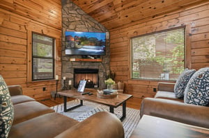 Cozy up in your rustic living room with warm wood walls, stone fireplace, and comfortable seating perfect for mountain getaway relaxation.