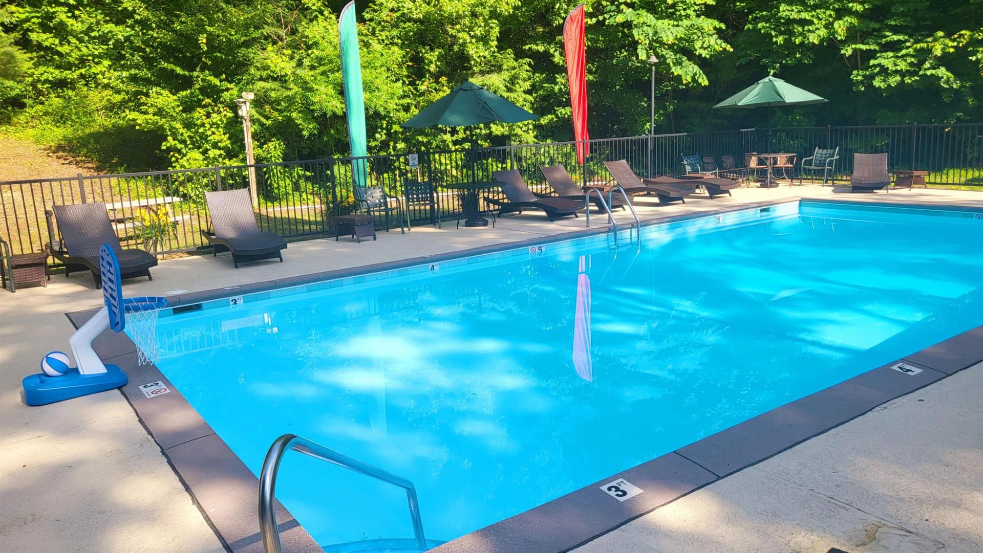 Sparkling outdoor pool surrounded by lush greenery, shaded lounge chairs, and vibrant umbrellas—perfect for sunny days and refreshing dips in a peaceful natural setting.