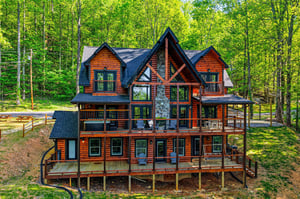Stunning log cabin retreat nestled among towering trees, featuring expansive decks and rustic charm in a peaceful forest setting.
