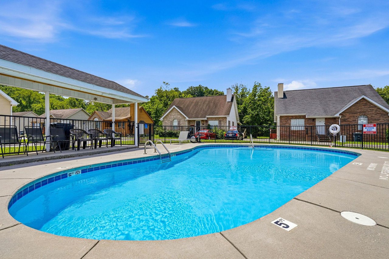 A sparkling outdoor pool surrounded by residential homes and lush trees, offering a perfect retreat for sunny days and warmweather relaxation.