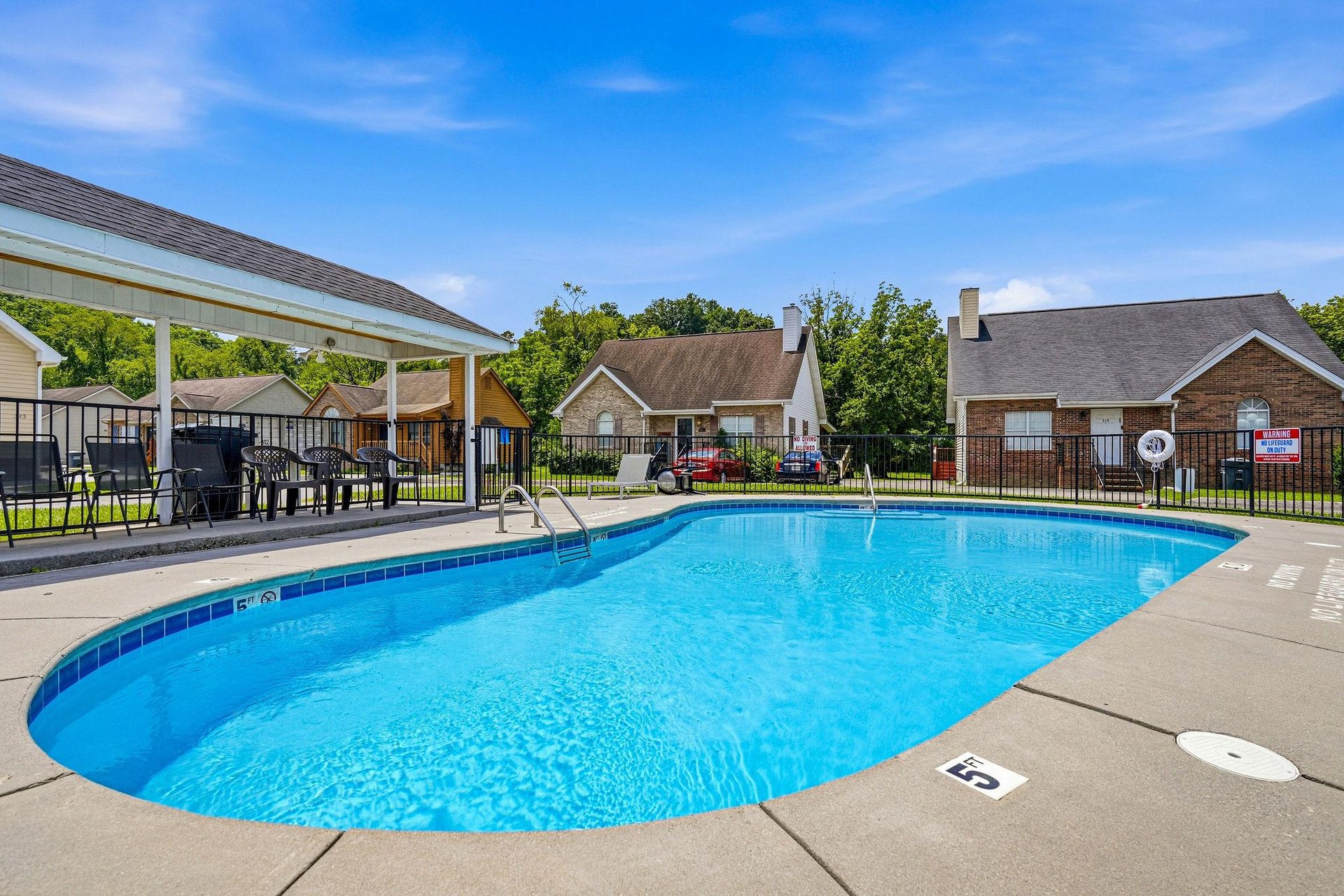 A sparkling outdoor pool surrounded by residential homes and lush trees, offering a perfect retreat for sunny days and warmweather relaxation.
