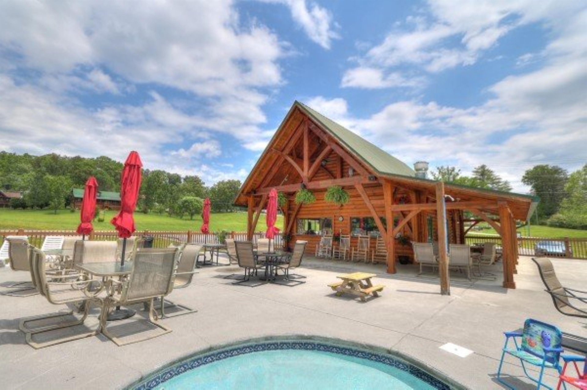 A covered outdoor pavilion features rustic log construction, offering shaded seating and dining areas beside the pool with mountain views beyond.