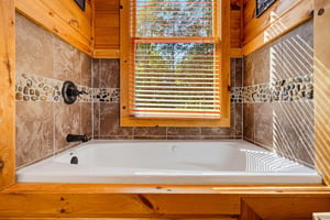 Sink into the deep soaking tub surrounded by warm wood and natural light streaming through the window. The stone tile and pebble accents create a peaceful spalike retreat.