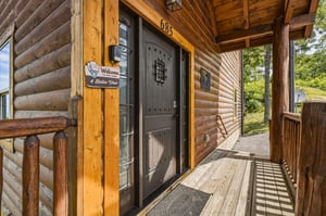 The log cabin entrance features a charming covered porch with rustic wooden beams, offering a welcoming arrival experience to your woodland retreat.