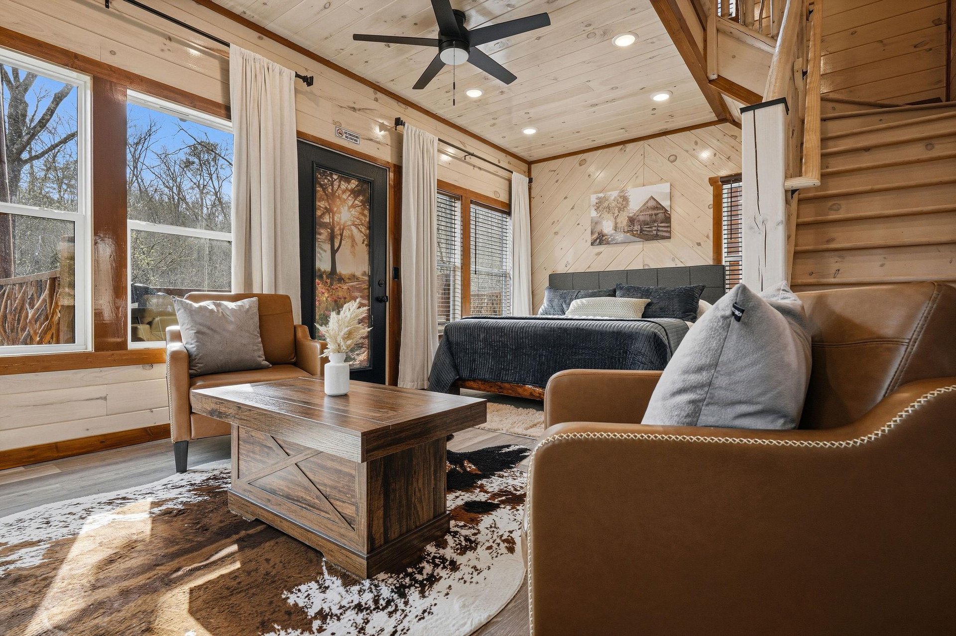 Unwind in your cozy cabin retreat with leather seating, rustic wood beams, and peaceful forest views streaming through oversized windows.