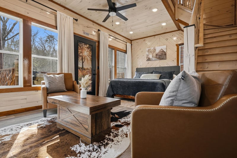 Unwind in your cozy cabin retreat with leather seating, rustic wood beams, and peaceful forest views streaming through oversized windows.