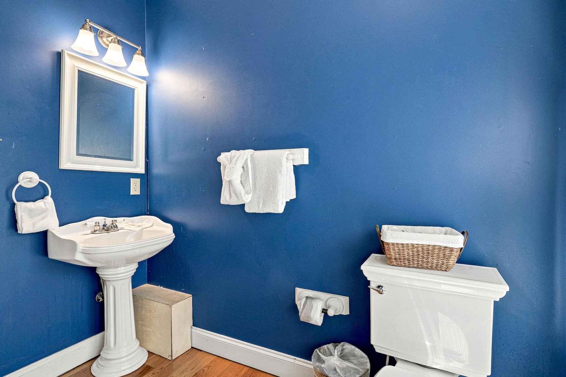 Your private bathroom features classic white fixtures against vibrant blue walls, with fresh towels ready for your use and thoughtful touches like a wicker basket for your convenience.