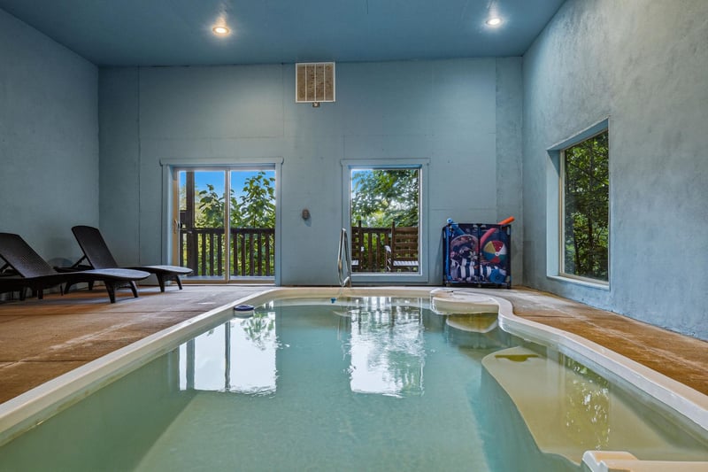 Slip into your private indoor pool surrounded by soothing blue walls and natural light streaming through windows overlooking lush greenery—your serene escape awaits.