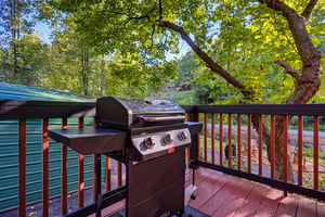 A gleaming stainless steel grill awaits on your private deck, surrounded by lush, sunlit foliage—perfect for afternoon cookouts and outdoor dining amidst serene natural beauty.