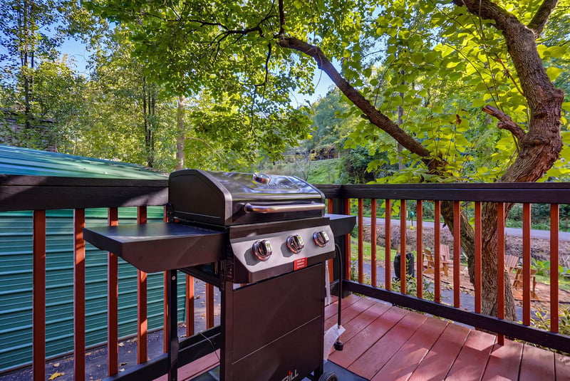 A gleaming stainless steel grill awaits on your private deck, surrounded by lush, sunlit foliage—perfect for afternoon cookouts and outdoor dining amidst serene natural beauty.