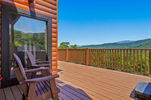 Soak in panoramic mountain views from your private deck, where cozy Adirondack chairs and a bubbling hot tub await your arrival under clear blue skies.