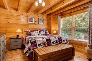 Unwind in your cozy bedroom, where rustic pine walls and vaulted ceilings create a warm, cabin retreat. Natural light pours through large windows as you relax on the plush bed after a day of adventure