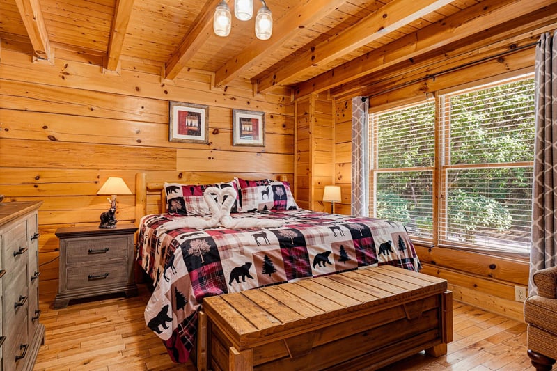 Unwind in your cozy bedroom, where rustic pine walls and vaulted ceilings create a warm, cabin retreat. Natural light pours through large windows as you relax on the plush bed after a day of adventure