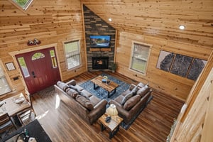 Relax in your spacious living room with soaring vaulted ceilings, warm wood walls, and a cozy stone fireplace. Sink into plush sofas, enjoy the TV above the hearth, and soak in natural light streaming